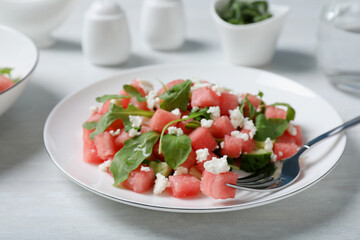 Delicious salad with watermelon, cucumber, arugula and feta cheese served on white wooden table, closeup