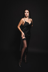 Fototapeta na wymiar full length view of sensual woman in satin dress and stockings standing on black