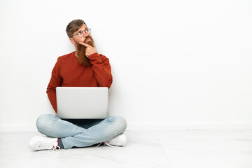 Young reddish caucasian man with laptop isolated on white background having doubts