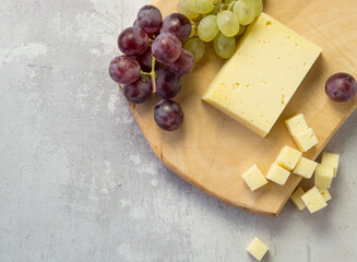 Light meal with sliced cheese next to a bunch of white and red grapes
