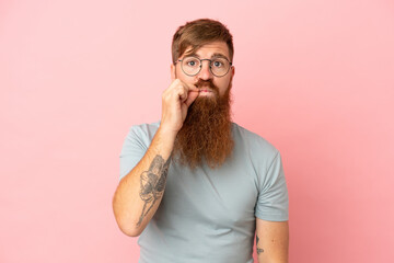 Young reddish caucasian man isolated on pink background showing a sign of silence gesture