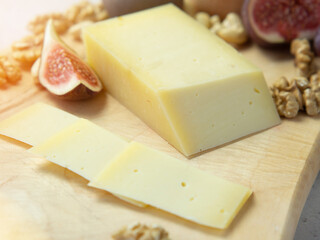 Slicing cheese with fruits - nuts and figs on a wooden board. Delicious snack