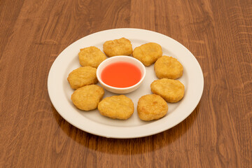 Portion of chicken nuggets battered in flour and egg with cheese sauce for dipping in a white plate on a dark wooden table.