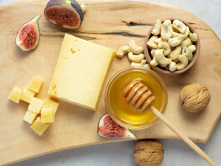 Pieces of aged cheese, nuts, figs and honey on a cutting board,