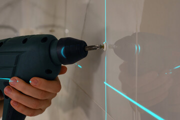 Woman using cross line laser level for accurate measurement and driving screw in tiled wall, closeup