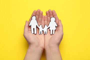 Woman holding paper family cutout on yellow  background, top view