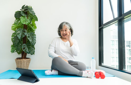 Senior Asian woman watching online courses on a laptop while exercising in the living room at home. Concept of workout training online.