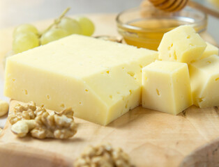 farm-quality cheese lies on a wooden board surrounded by grapes. nuts and honey close-up on a light background