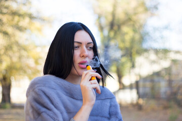 The girl smokes an electronic cigarette in the fresh air.
