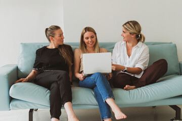 three young attractive women at home on the couch talking while looking at the laptop