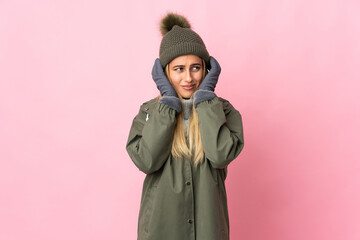 Young woman with winter hat isolated on pink background frustrated and covering ears