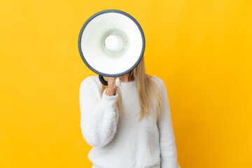 Young blonde woman isolated on yellow background shouting through a megaphone to announce something