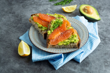 Toasts with avocado and smoked salmon on gray background, copy space. Healthy food.