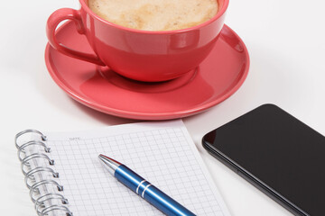 Mobile phone, coffee with milk and notepad for writing notes. White background