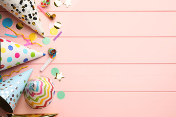 Flat lay composition with party hats, blowers and confetti on light pink wooden background. Space...