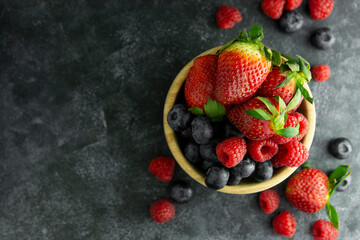 Assortment berries blueberries, strawberries and raspberries in wooden bowl. Dark moody background.