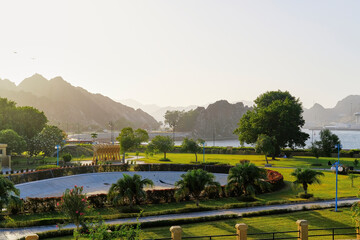 Park with a green lawn and big trees, mountain and sky background, Oman Muscat tourism, no people.