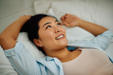 Fototapeta na wymiar Young happy Asian woman day dreaming while relaxing on bed at home.