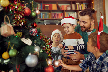 Happy father and his sons enjoy in decorating Christmas tree together at home.