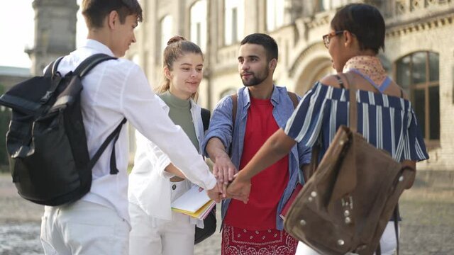 Multiethnic college students stacking hands in slow motion laughing standing at university campus outdoors. Happy confident young beautiful women and handsome men studying in university