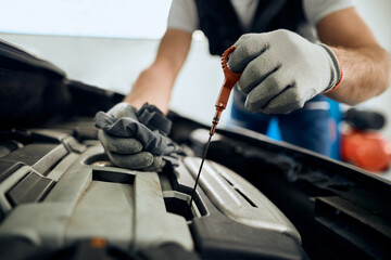 Close-up of car mechanic checks oil level during engine maintenance at service workshop.