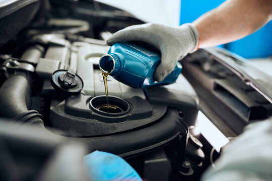 Close- up of mechanic pours motor oil while doing car engine maintenance at auto repair shop.