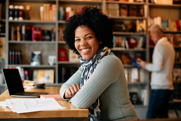 Happy mid adult black woman studies at university library and looks at camera.