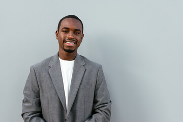 Positive black man in formal outfit standing near gray wall