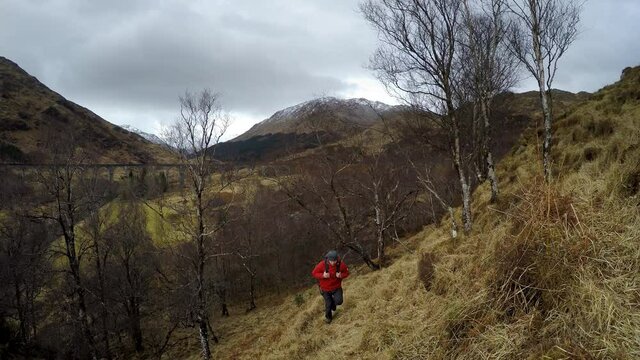 4K footage of a backpacker traveler dressed red windproof softshell jacket exploring the hills near the famous Glenfinnan Viaduct in the Northern Scotland.