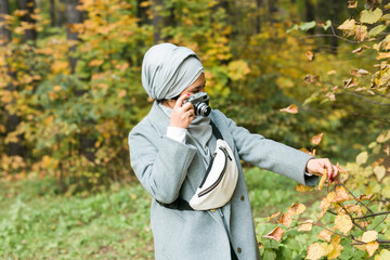 Young Arab Woman wearing hijab headscarf photographing with a smartphone in park. Modern muslim girl