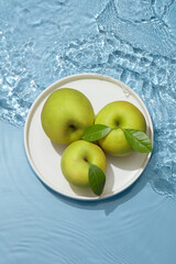 Transparent blue colored clear water surface texture with ripples, splashes and bubbles , Abstract nature blue background Water waves in sunlight with apple template in dish for cosmetic advertising