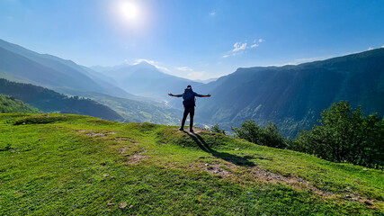 A man with big hiking backpack spreading his arms wide open, while standing on the mountain peak,...