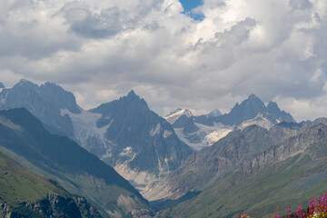 Fototapeta premium A panoramic view on high Caucasus mountains in Georgia. There are high, snowcapped peaks in the back. Thick clouds above the peaks. Idyllic landscape. Calmness and meditation. Natural remedy