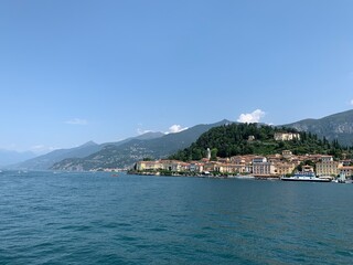 Fototapeta na wymiar View of Bellagio city skyline from arriving boat. Varenna town and mountains in the background. Bellagio is a famous sightseeing and tourism place at Lago di Como. Bellagio, Como Lake, Italy