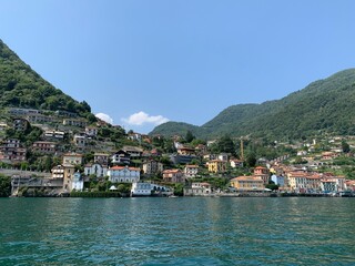Fototapeta premium Skyline of Argegno town with houses on hills and mountains. Landscape of Como Lake (Lago di Como) shore. View from the boat. It is a famous Italian vacation place. Argegno, Como Lake, Lombardy, Italy.