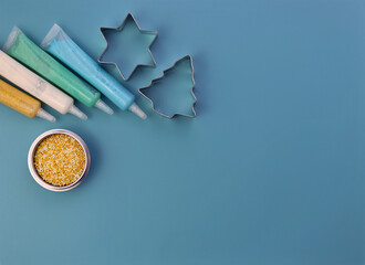 Colored sugar decoration and steel cookie cutters on a blue background. Tubes of paint and small...