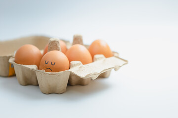 Brown eggs arranged in a box with a sad, lonely face.