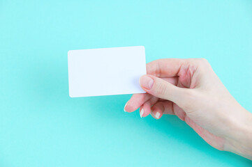 White plastic card in the hand of a Caucasian woman on turquoise background. Place for your text.