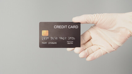 Hand is wear WHITE medical glove and holding black credit card isolated on grey background.