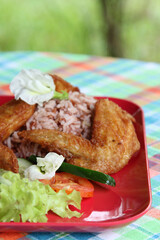 Thai style food, the deep fried chicken wings with rice, soup, vegetable and fruit on red plate.