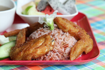 Thai style food, the deep fried chicken wings with rice, soup, vegetable and fruit on red plate.