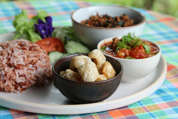 Thai style food, rice with stir fried basil with pork, chili paste, pork kappa and vegetable on white plate.