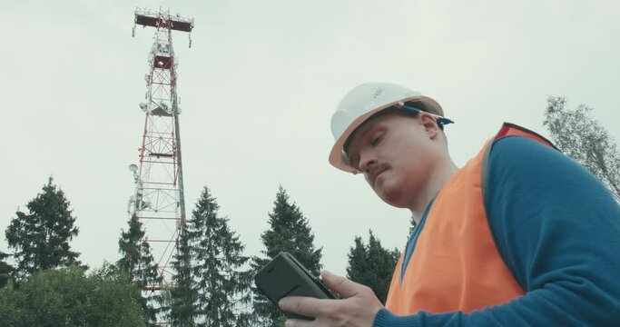 4G and 5G cellular radio tower, worker in workwear and helmet is standing next to it. Installing new cellular and Internet communication towers around world. Repair and maintenance