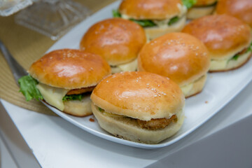 Beautifully decorated catering banquet table with different hamburgers burgers sandwiches on a plate on corporate birthday . Mini or Small Burger Canape in Luxury Restaurant for Brunch Time .