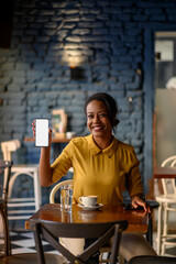 Beautiful young african american woman showing a smartphone while sitting in a cafe