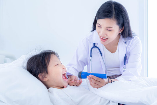 Medical Pediatrician Doctor In White Uniform Gown Use Hand Open Mouth Of Children, She Use Flashlight And Diagnosis In Hospital.