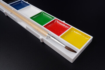 watercolor paints and a brush lie on a black background