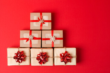 Christmas gifts are laid out in the form of a tree on a red background. Gifts in kraftkoroboki and kraft paper with bows