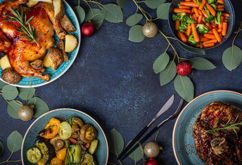 Christmas evening table top view with assorted festive food, baked chicken, roasted ham, vegetables decorated with Xmas toys and eucalyptus branches, space for text background

