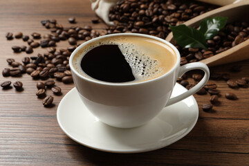 Cup of aromatic hot coffee and beans on wooden table, closeup